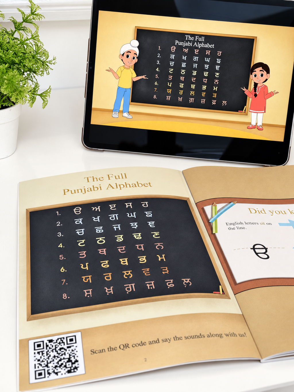 An open book showing the Full Punjabi Alphabet with a blackboard-style page and QR code, alongside a tablet displaying the same educational content. The scene is styled on a white surface with a small potted plant at the side.